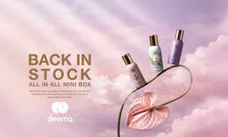 Three mini hair care bottles from deema are arranged on a curved green stem against a pink cloudy sky background. The bottles are labeled All In, Volatile, and Pink, with gold caps.